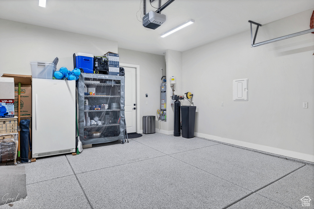 Garage with electric panel, a garage door opener, and white fridge