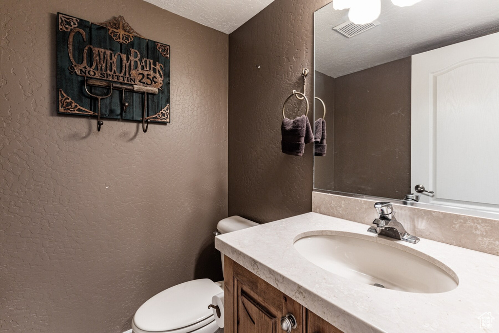 Bathroom with a textured ceiling, vanity, and toilet