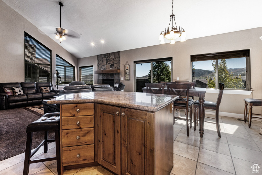 Kitchen featuring pendant lighting, ceiling fan with notable chandelier, lofted ceiling, light tile patterned floors, and a stone fireplace