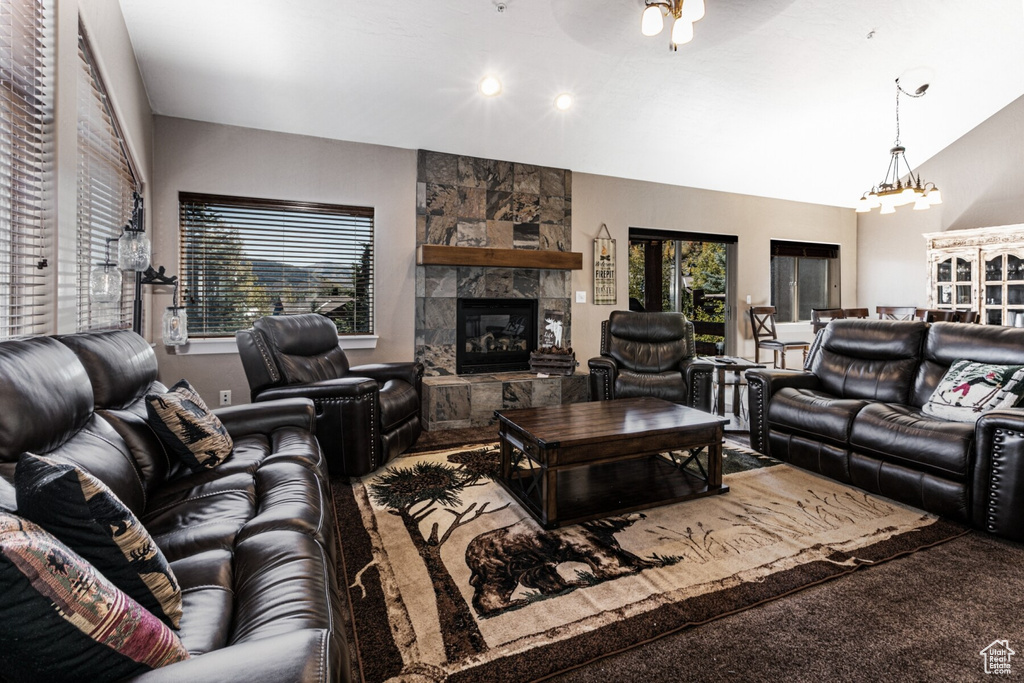 Carpeted living room with ceiling fan with notable chandelier, a wealth of natural light, vaulted ceiling, and a large fireplace