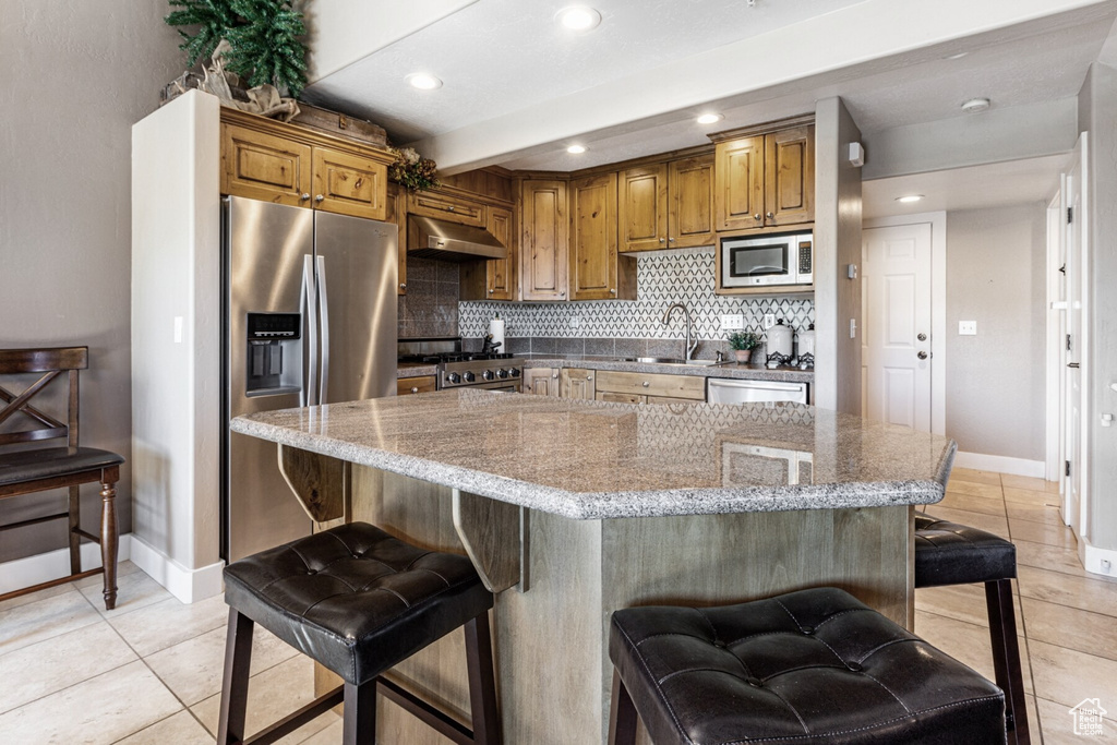 Kitchen featuring a breakfast bar, backsplash, a kitchen island, stainless steel appliances, and extractor fan