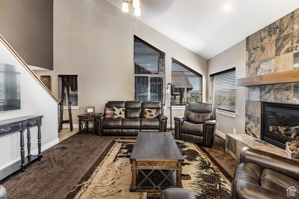 Living room featuring lofted ceiling, ceiling fan, a fireplace, and carpet flooring