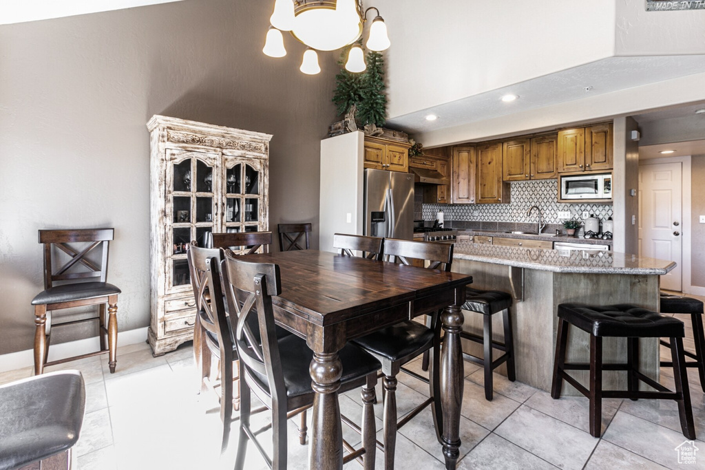 Dining room featuring a towering ceiling, sink, light tile patterned floors, and a notable chandelier