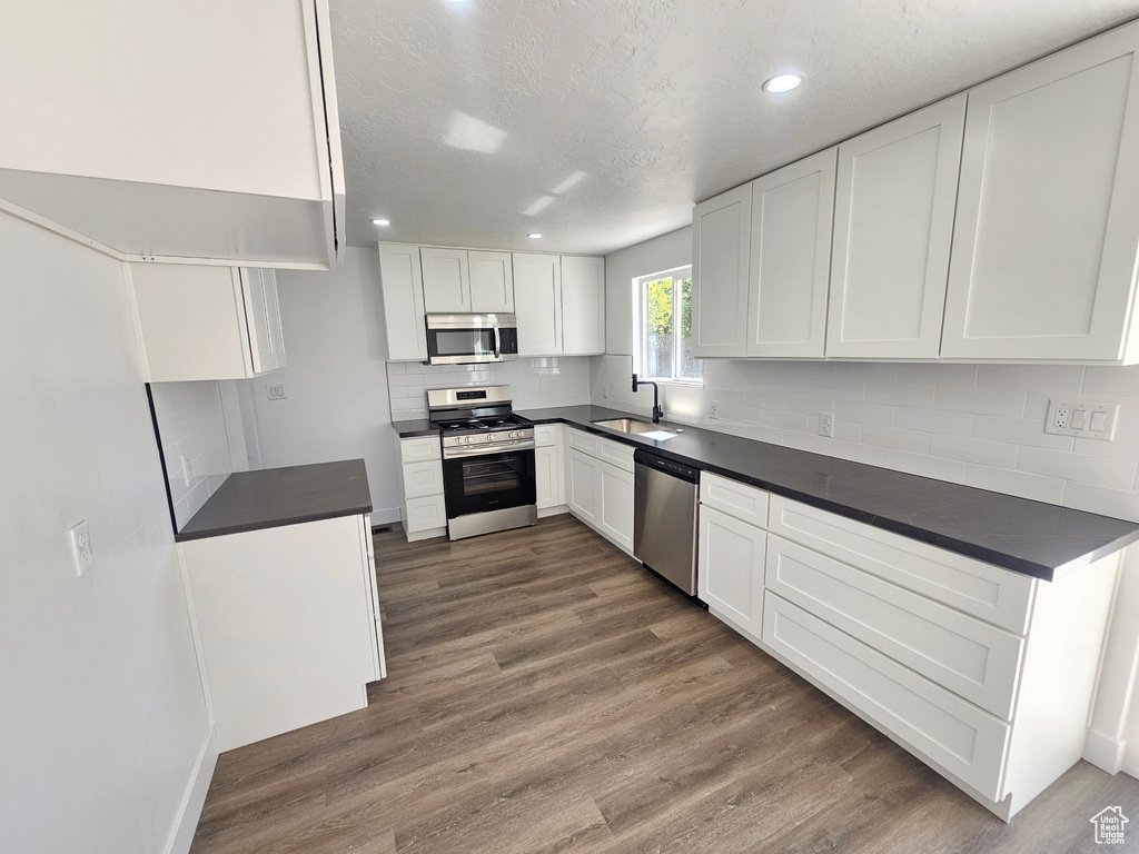 Kitchen with sink, appliances with stainless steel finishes, dark wood-type flooring, and white cabinetry