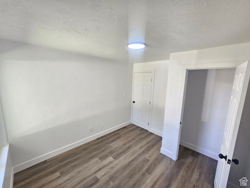 Unfurnished bedroom with a textured ceiling, dark hardwood / wood-style floors, and a closet