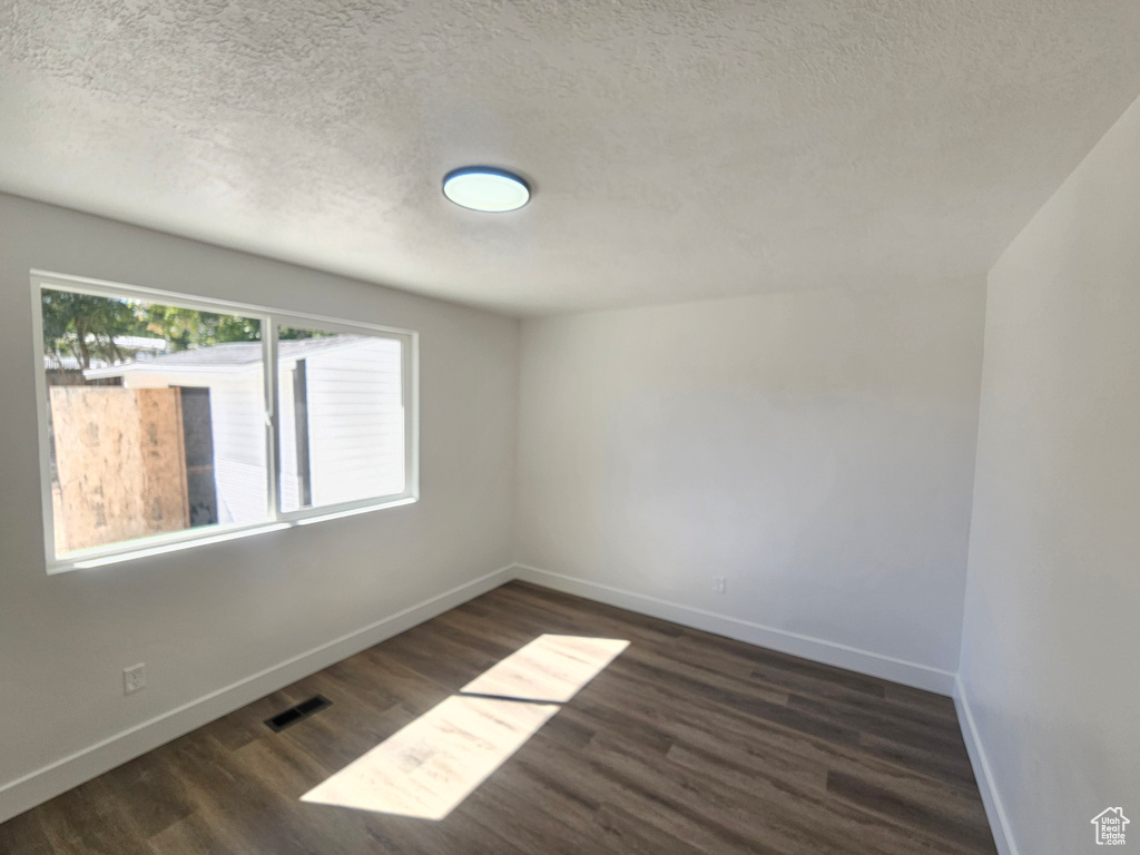 Empty room featuring a textured ceiling and dark wood-type flooring