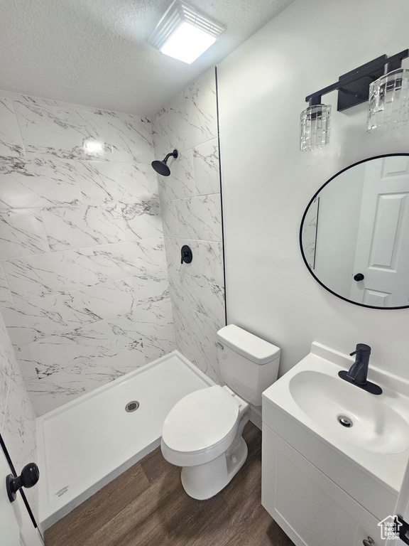 Bathroom featuring tiled shower, vanity, a textured ceiling, hardwood / wood-style flooring, and toilet