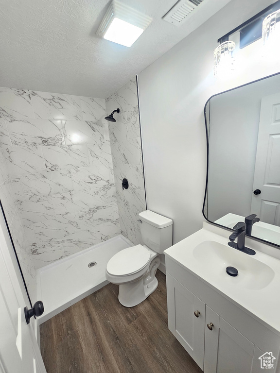 Bathroom with a tile shower, vanity, toilet, and wood-type flooring