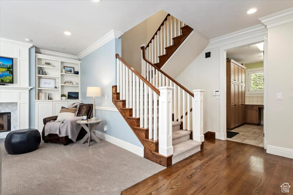 Stairway featuring wood-type flooring, crown molding, and a high end fireplace