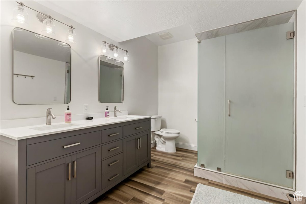 Bathroom with vanity, wood-type flooring, a textured ceiling, a shower with shower door, and toilet