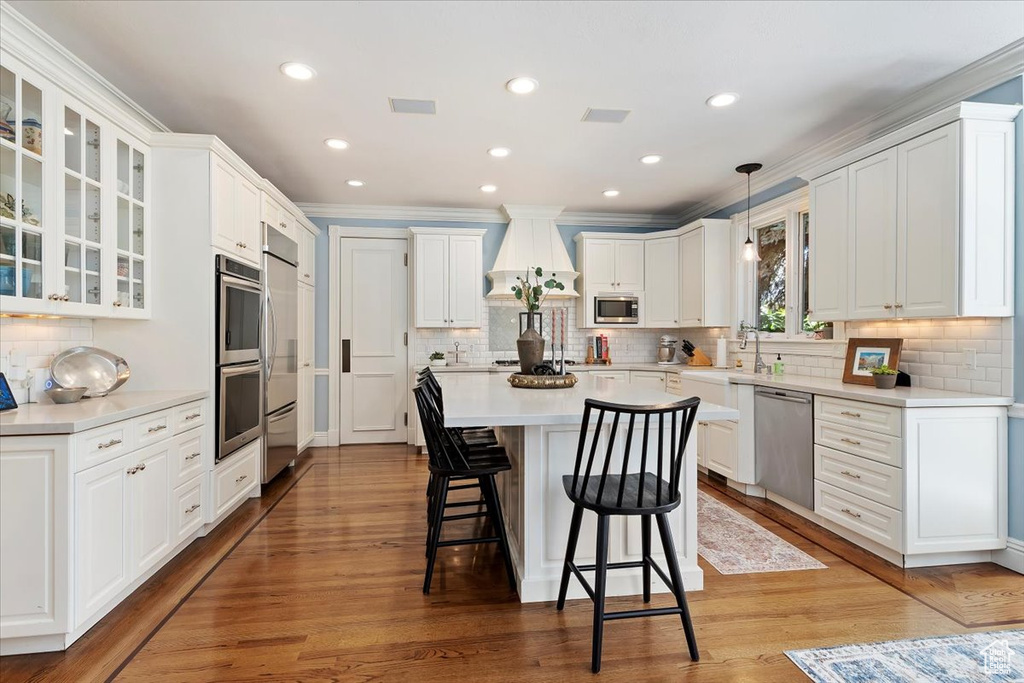 Kitchen with white cabinets, built in appliances, decorative light fixtures, and light hardwood / wood-style floors