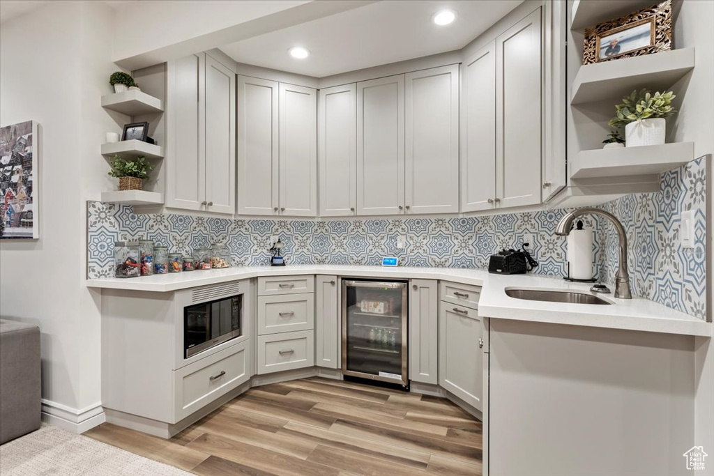 Kitchen featuring light hardwood / wood-style floors, tasteful backsplash, sink, beverage cooler, and stainless steel microwave