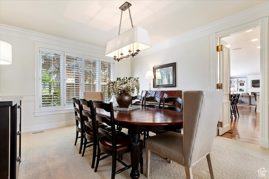 Carpeted dining space with an inviting chandelier and ornamental molding