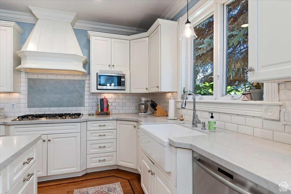 Kitchen featuring pendant lighting, stainless steel appliances, white cabinetry, and custom exhaust hood