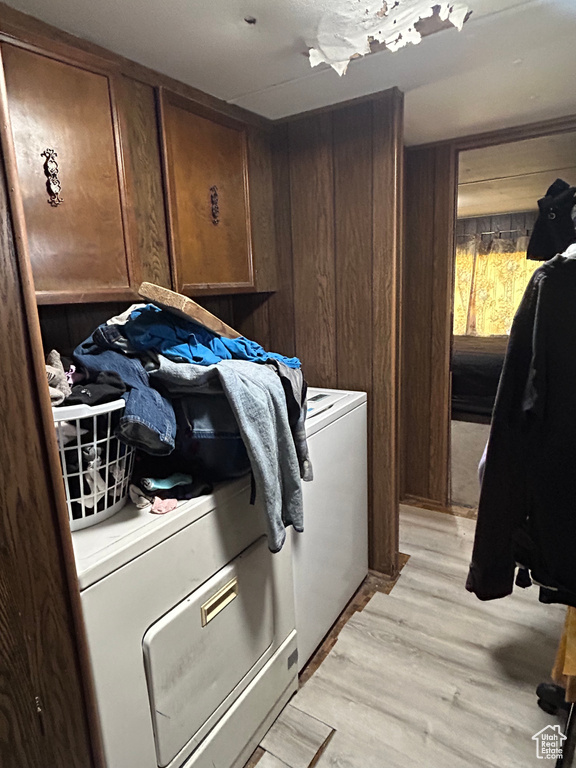 Clothes washing area with light wood-type flooring, washer and dryer, and wooden walls