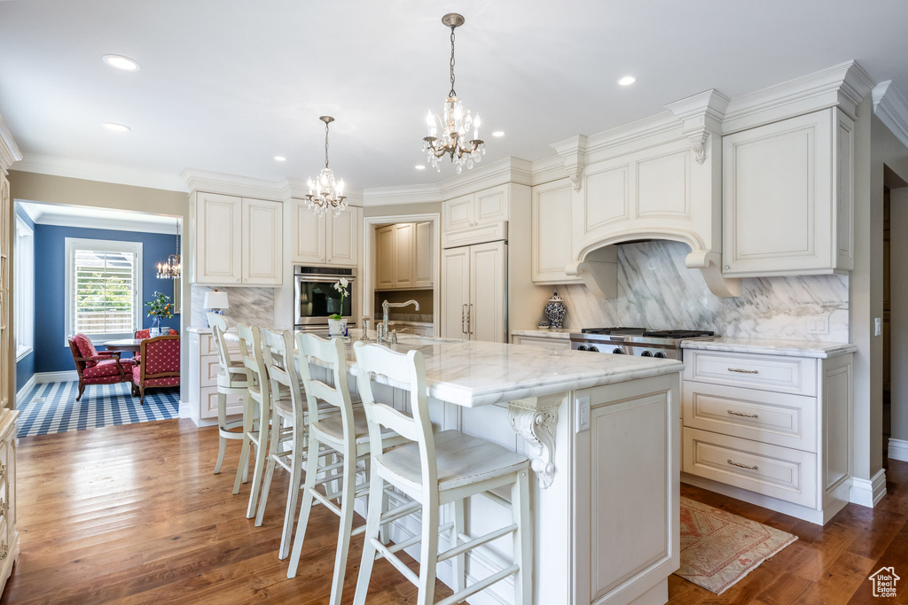 Kitchen featuring pendant lighting, light stone counters, dark hardwood / wood-style floors, decorative backsplash, and a center island with sink