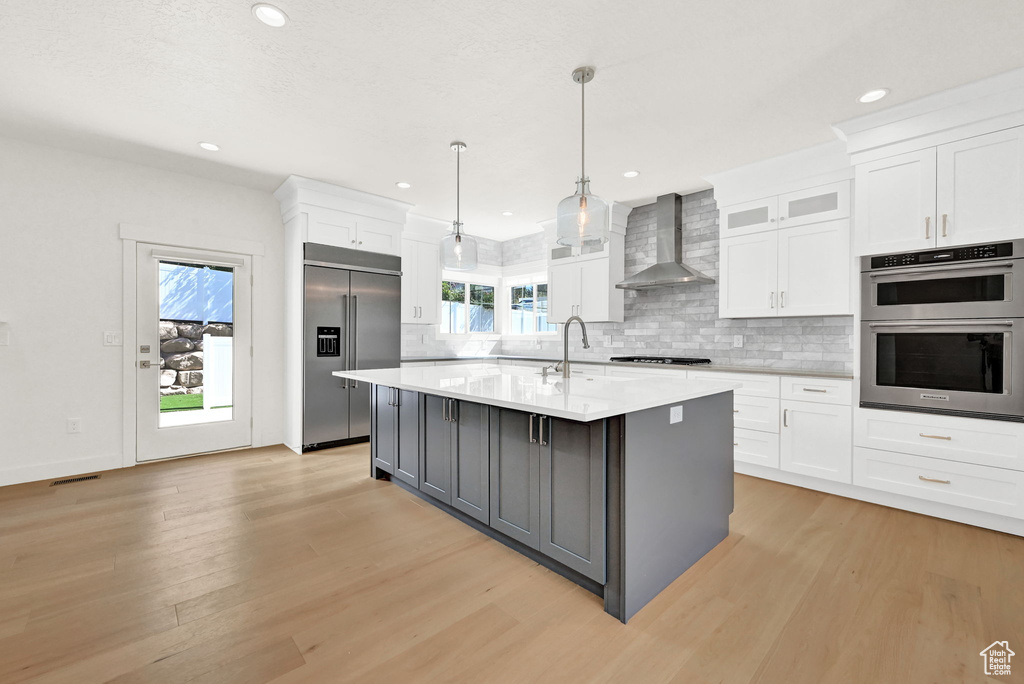 Kitchen featuring wall chimney exhaust hood, stainless steel appliances, white cabinetry, and a wealth of natural light