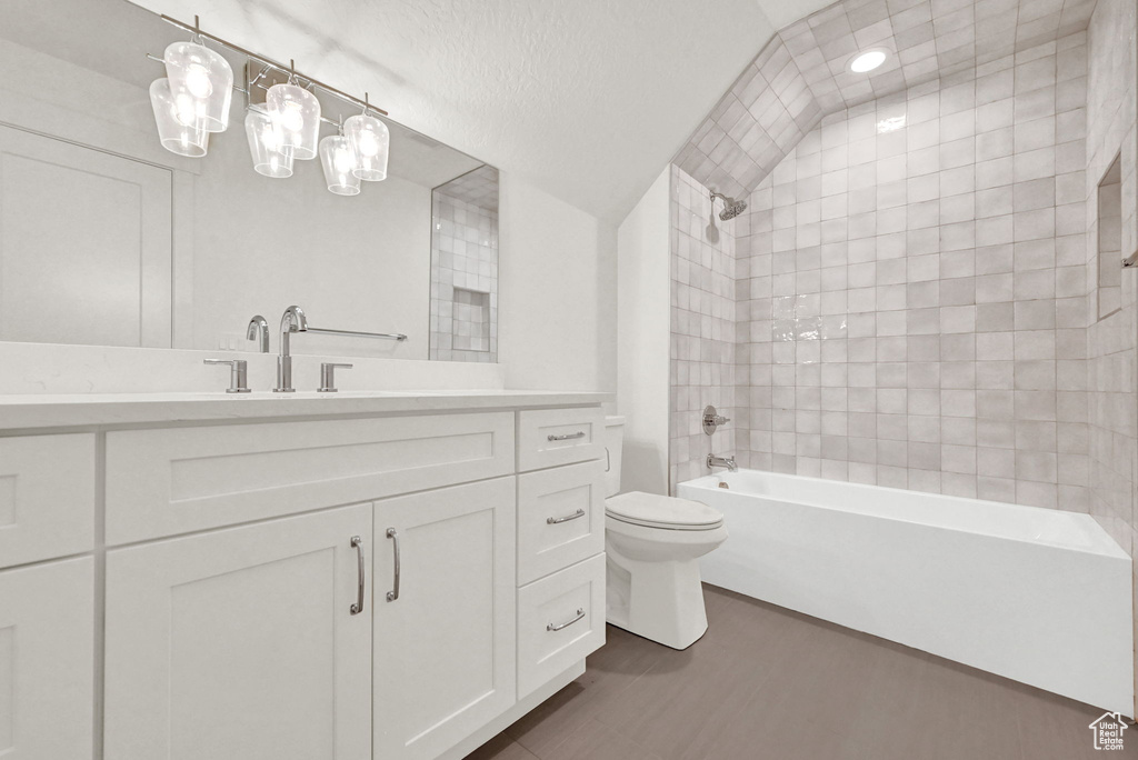 Full bathroom with a textured ceiling, lofted ceiling, tiled shower / bath combo, vanity, and toilet