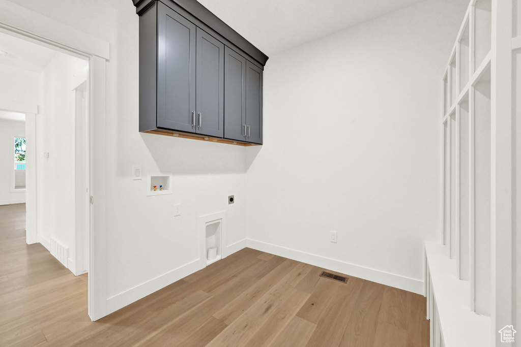 Laundry room featuring hookup for a washing machine, light hardwood / wood-style floors, electric dryer hookup, and cabinets