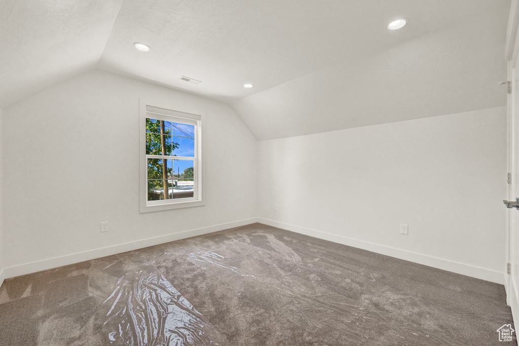 Additional living space with a textured ceiling, vaulted ceiling, and carpet