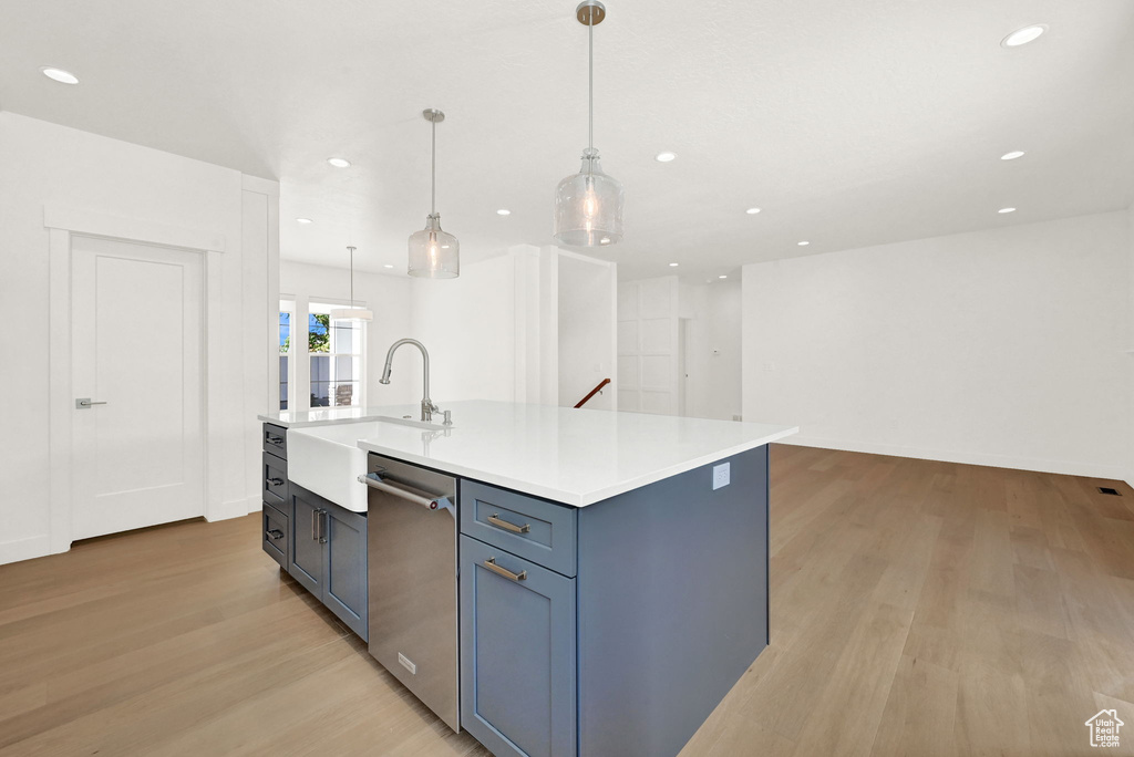 Kitchen featuring hanging light fixtures, light hardwood / wood-style floors, stainless steel dishwasher, a kitchen island with sink, and sink