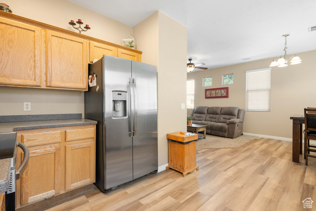 Kitchen with light brown cabinets, hanging light fixtures, light hardwood / wood-style flooring, stainless steel appliances, and ceiling fan with notable chandelier