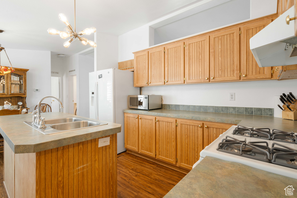 Kitchen with white appliances, dark hardwood / wood-style flooring, a center island with sink, sink, and a notable chandelier