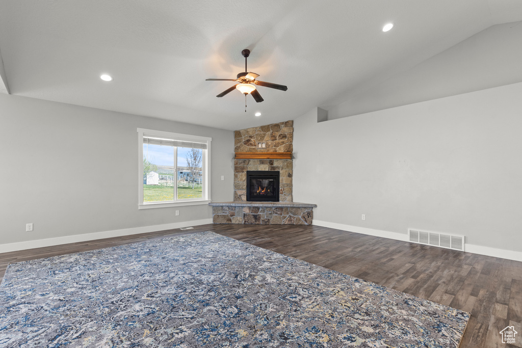 Unfurnished living room featuring ceiling fan, vaulted ceiling, wood finished floors, a fireplace, and baseboards