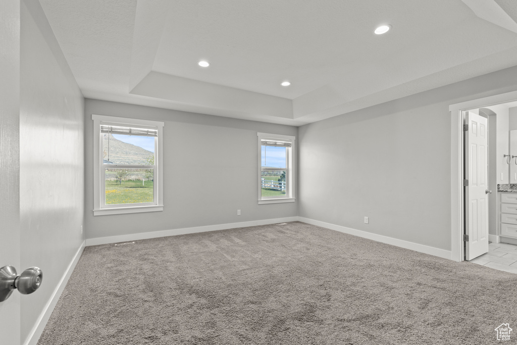 Carpeted empty room featuring baseboards, a raised ceiling, and recessed lighting