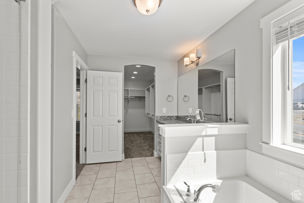 Full bathroom featuring a walk in closet, tile patterned flooring, a bath, and baseboards
