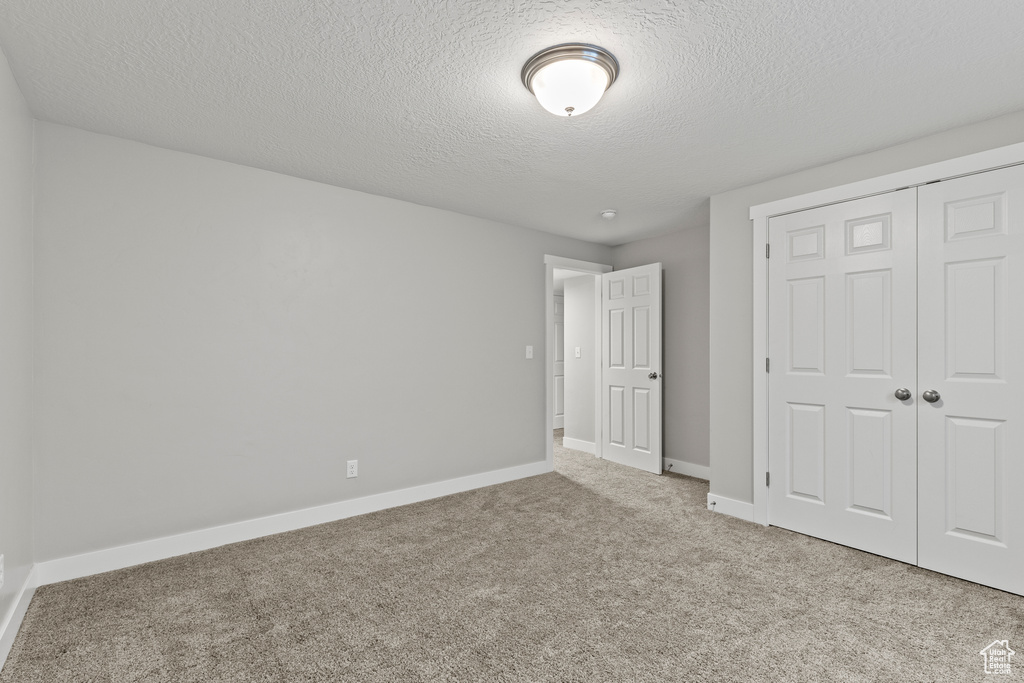 Unfurnished bedroom with a textured ceiling, carpet, a closet, and baseboards