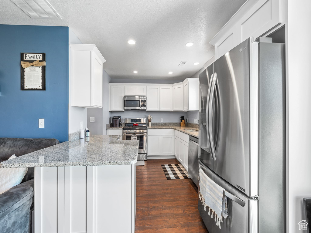 Kitchen with dark hardwood / wood-style floors, white cabinetry, kitchen peninsula, a kitchen breakfast bar, and stainless steel appliances