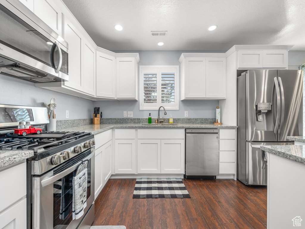 Kitchen featuring appliances with stainless steel finishes, light stone countertops, dark wood-type flooring, and white cabinets