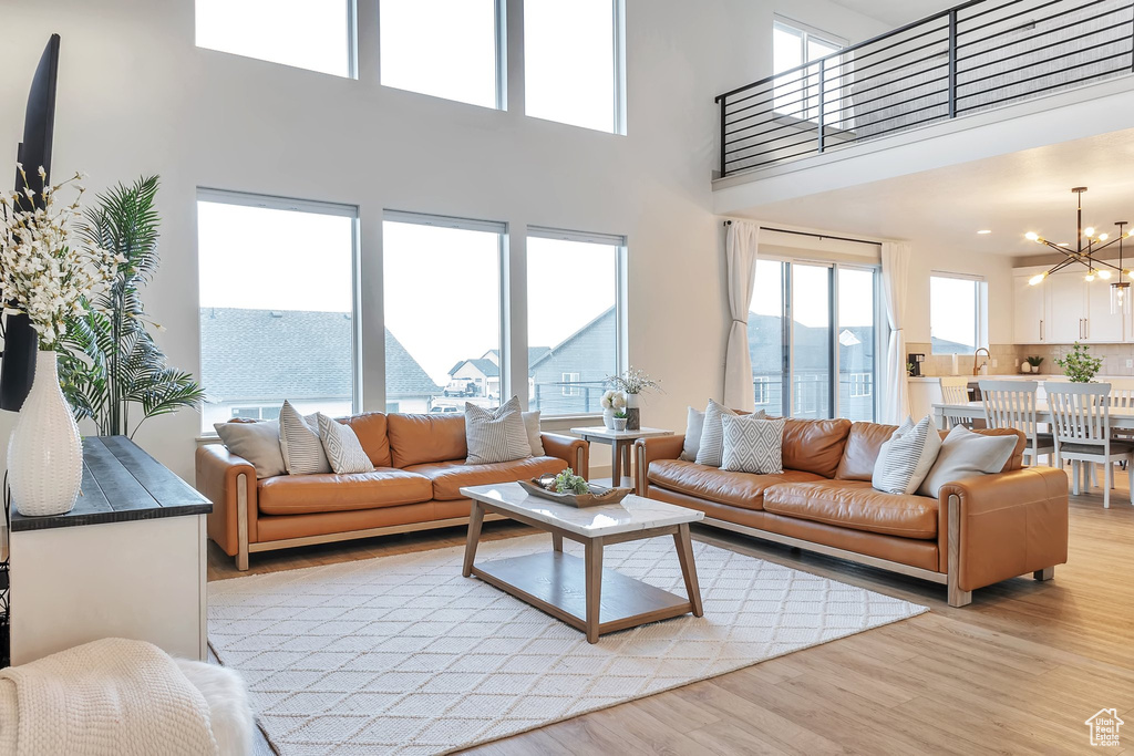 Living room featuring a notable chandelier, a wealth of natural light, a towering ceiling, and light hardwood / wood-style flooring