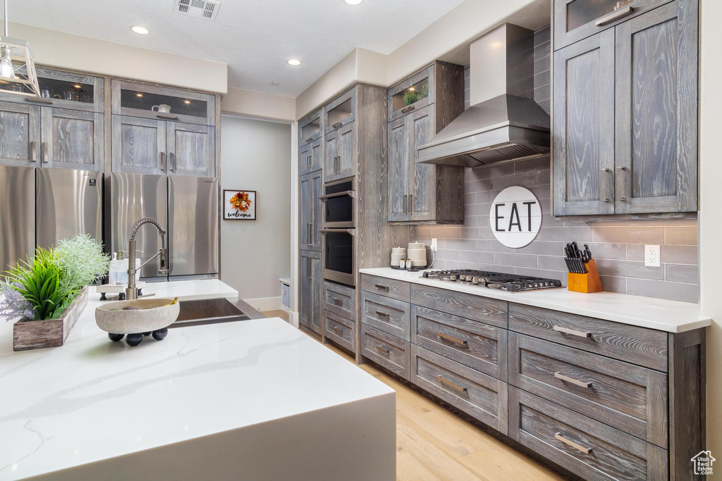 Kitchen with light hardwood / wood-style floors, wall chimney exhaust hood, sink, and light stone counters