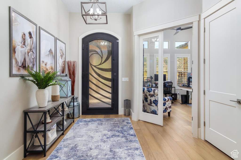 Foyer entrance with light wood-type flooring and ceiling fan with notable chandelier