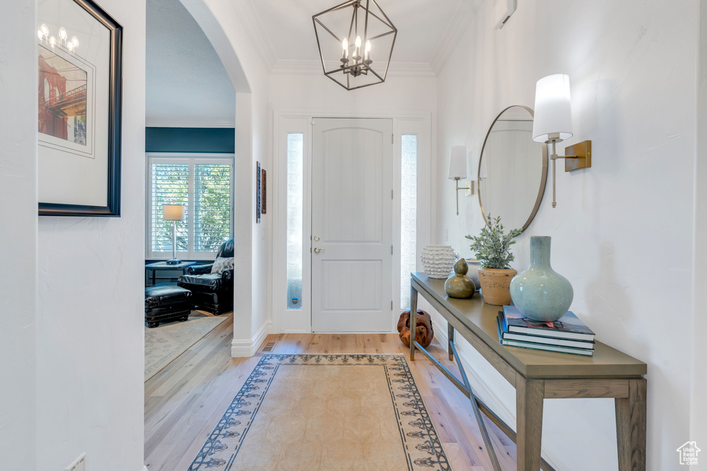 Foyer entrance with light hardwood / wood-style flooring, a chandelier, and crown molding