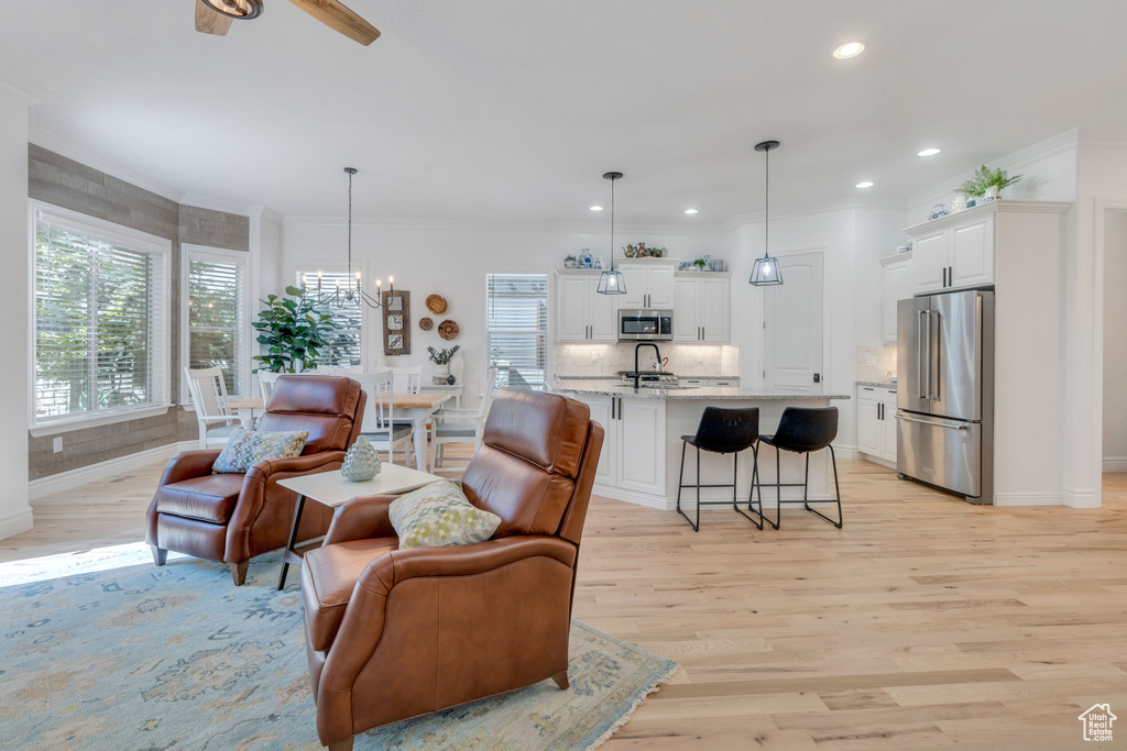 Living room featuring ceiling fan with notable chandelier, light hardwood / wood-style floors, ornamental molding, and sink