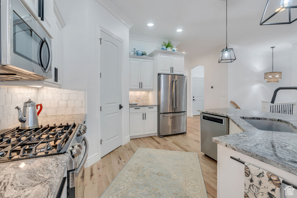 Kitchen featuring white cabinets, sink, decorative light fixtures, stainless steel appliances, and light stone countertops