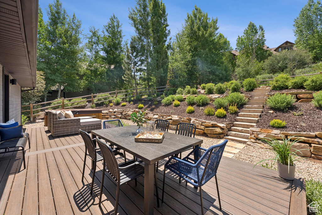 Wooden terrace featuring stairway, outdoor dining area, and view of wooded area