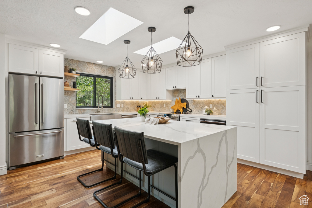 Kitchen with high end fridge, a skylight, light wood finished floors, white cabinets, and recessed lighting