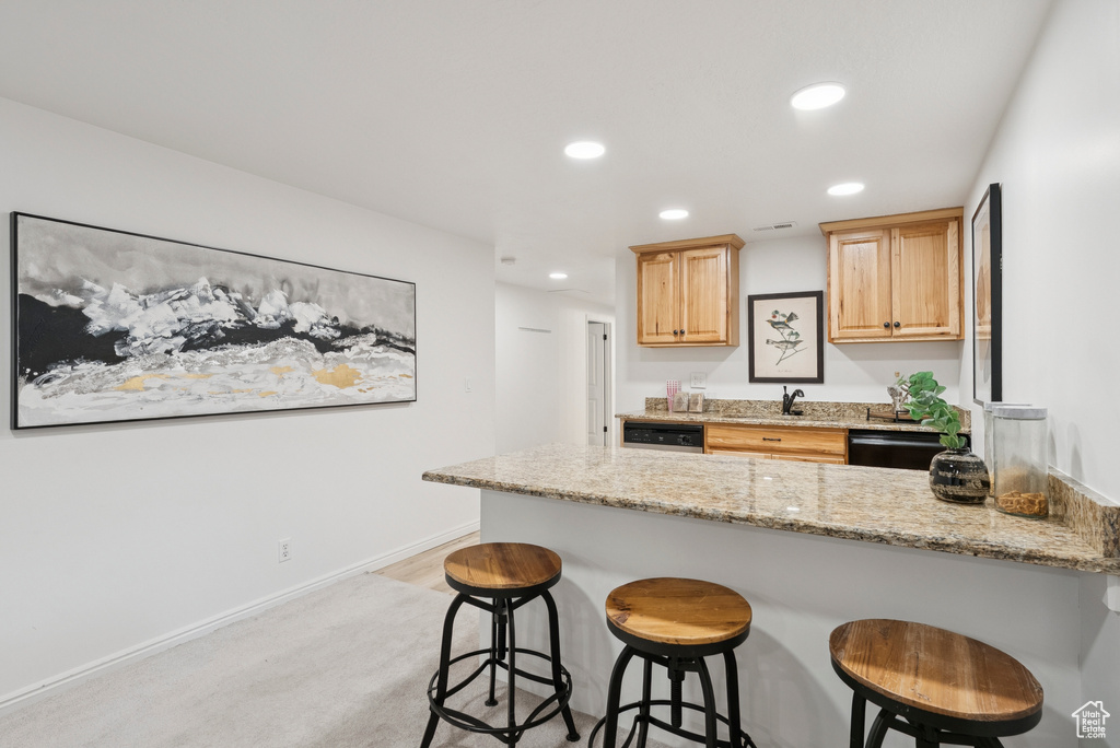 Kitchen featuring a peninsula, a breakfast bar, recessed lighting, light stone countertops, and dishwasher
