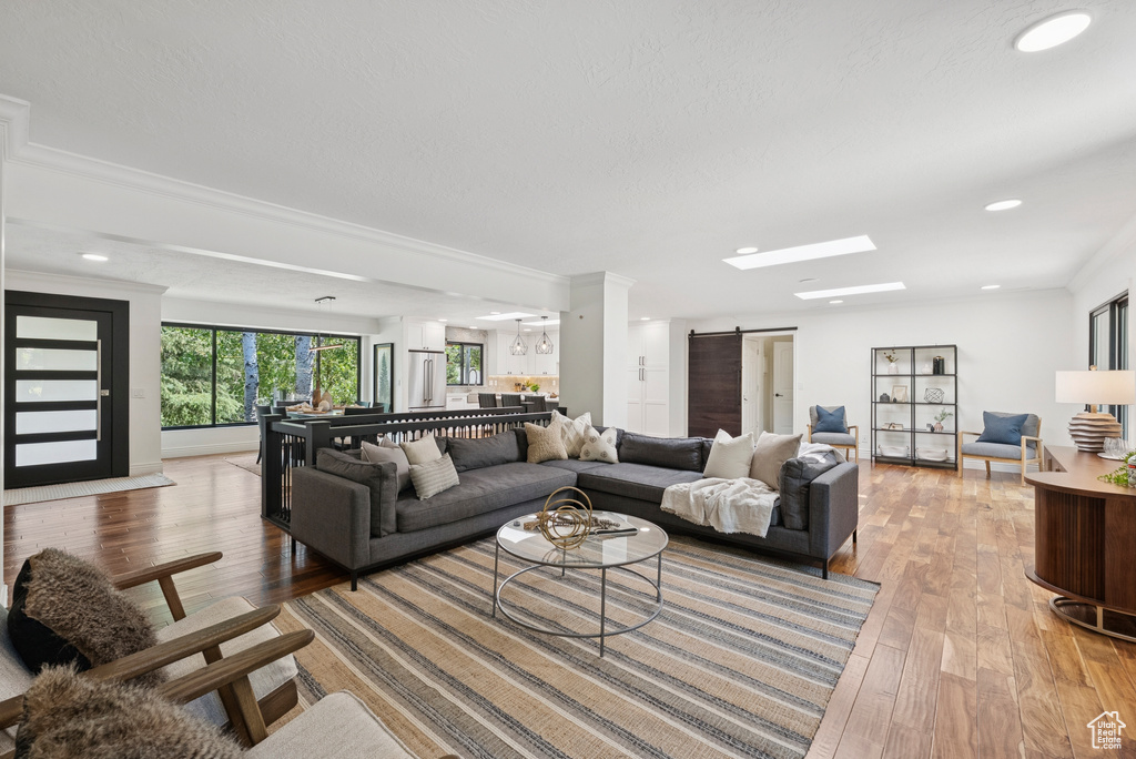 Living room featuring light wood-style floors, crown molding, a barn door, and recessed lighting