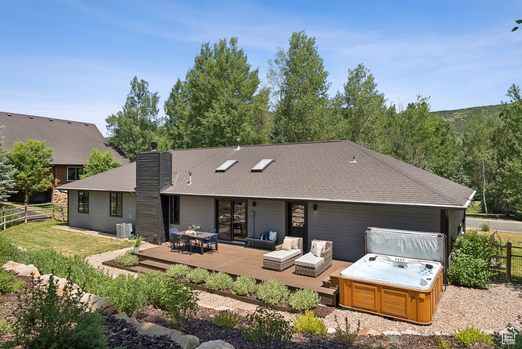Rear view of property featuring a hot tub, a wooden deck, a chimney, outdoor lounge area, and roof with shingles