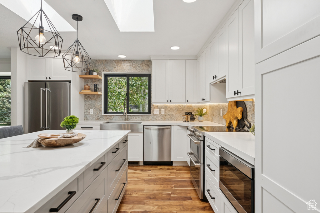 Kitchen with high quality appliances, light wood-style floors, white cabinetry, recessed lighting, and decorative backsplash