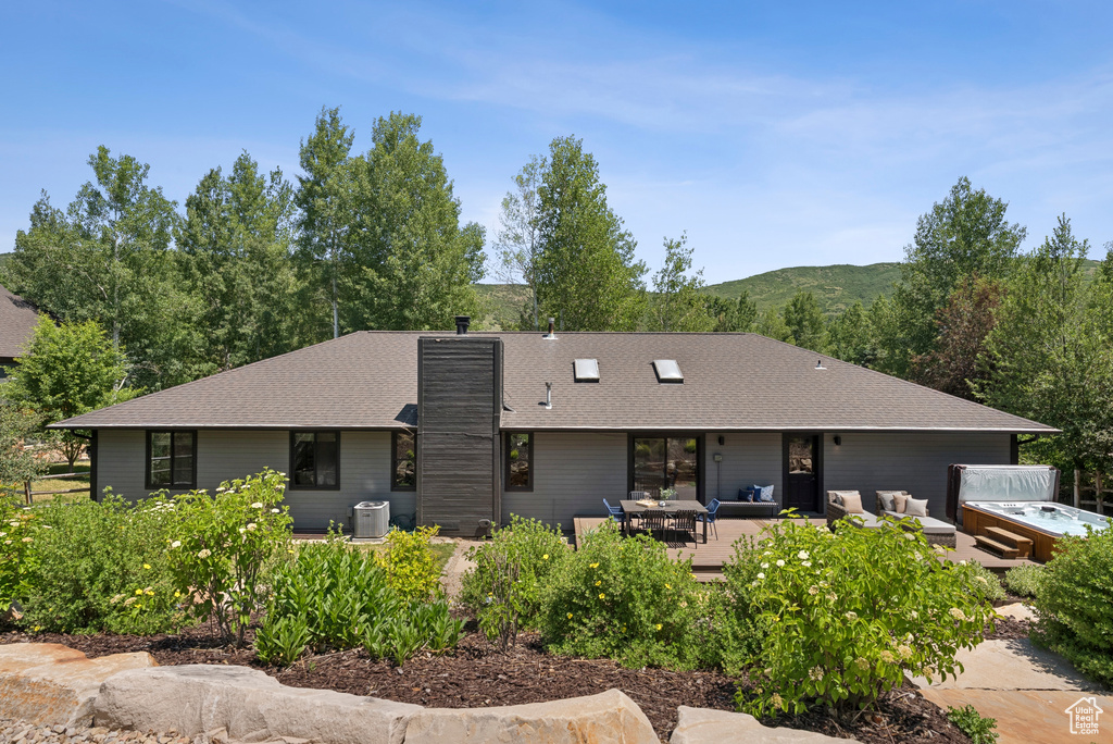 Back of property with a hot tub, a chimney, an outdoor living space, roof with shingles, and a patio