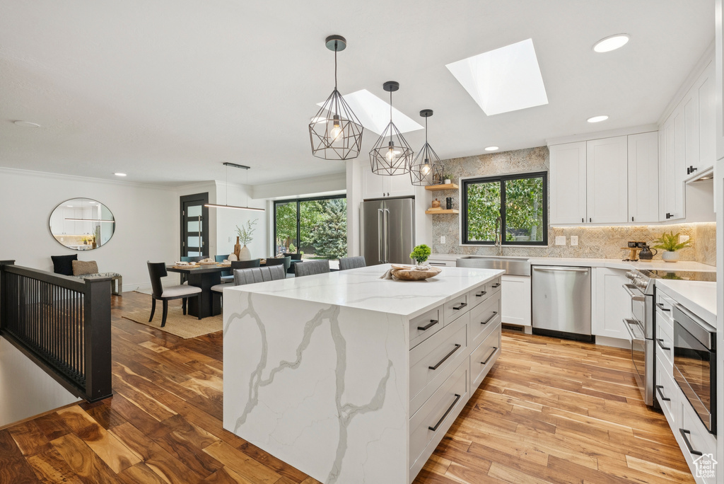 Kitchen with premium appliances, decorative backsplash, light wood-style floors, a skylight, and white cabinets