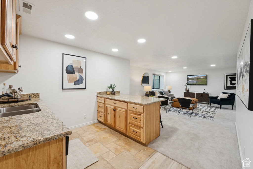 Kitchen with a peninsula, recessed lighting, light stone countertops, open floor plan, and a breakfast bar