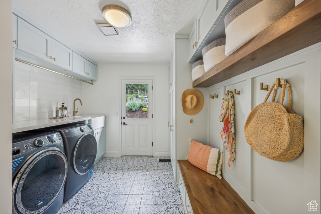 Clothes washing area with a textured ceiling, light tile patterned floors, independent washer and dryer, and cabinets