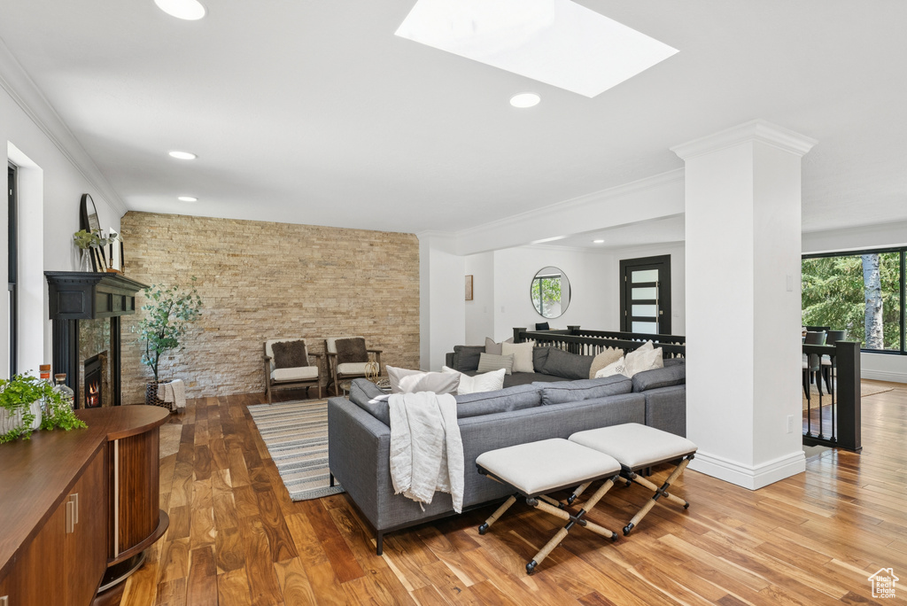 Living room with light wood-type flooring, recessed lighting, ornamental molding, a skylight, and a warm lit fireplace